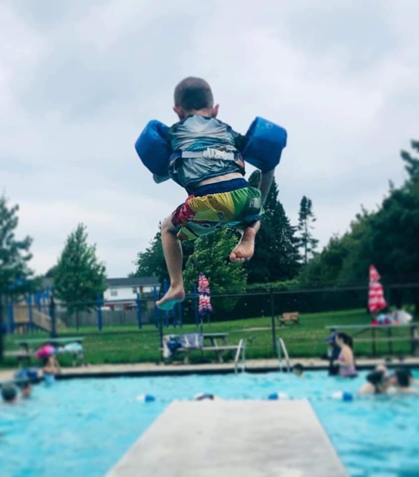 boy jumping off diving board with floaties on into Forest Edge Community Pool